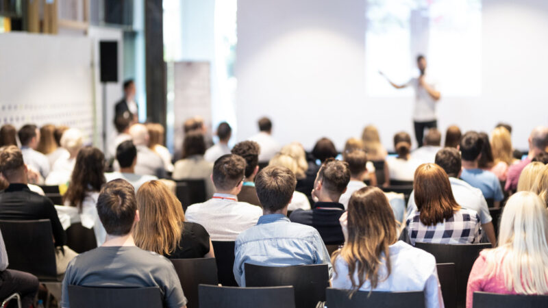 Speaker giving a talk in conference hall at business event. Audience at the conference hall. Business and Entrepreneurship concept. Focus on unrecognizable people in audience.