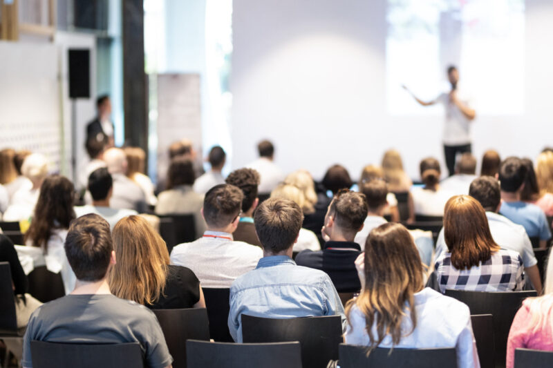 Speaker giving a talk in conference hall at business event. Audience at the conference hall. Business and Entrepreneurship concept. Focus on unrecognizable people in audience.